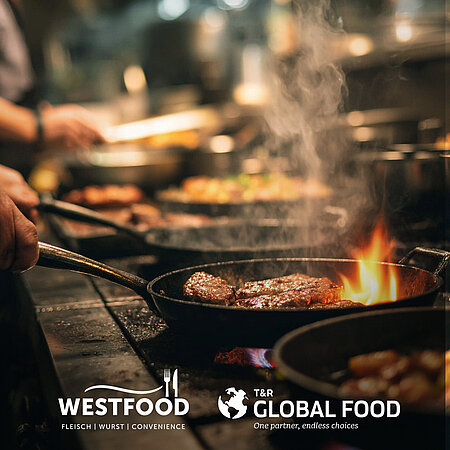 In einer Küche mit dunkler, edler Arbeitsplatte wird im Vordergrund Fleisch in einer gusseiserner Pfanne gebraten. Im Hintergrund werden weitere Gerichte zubereitet. Unten auf dem Bild sind die Logos von WestFood und Global Food in weiß zu sehen.